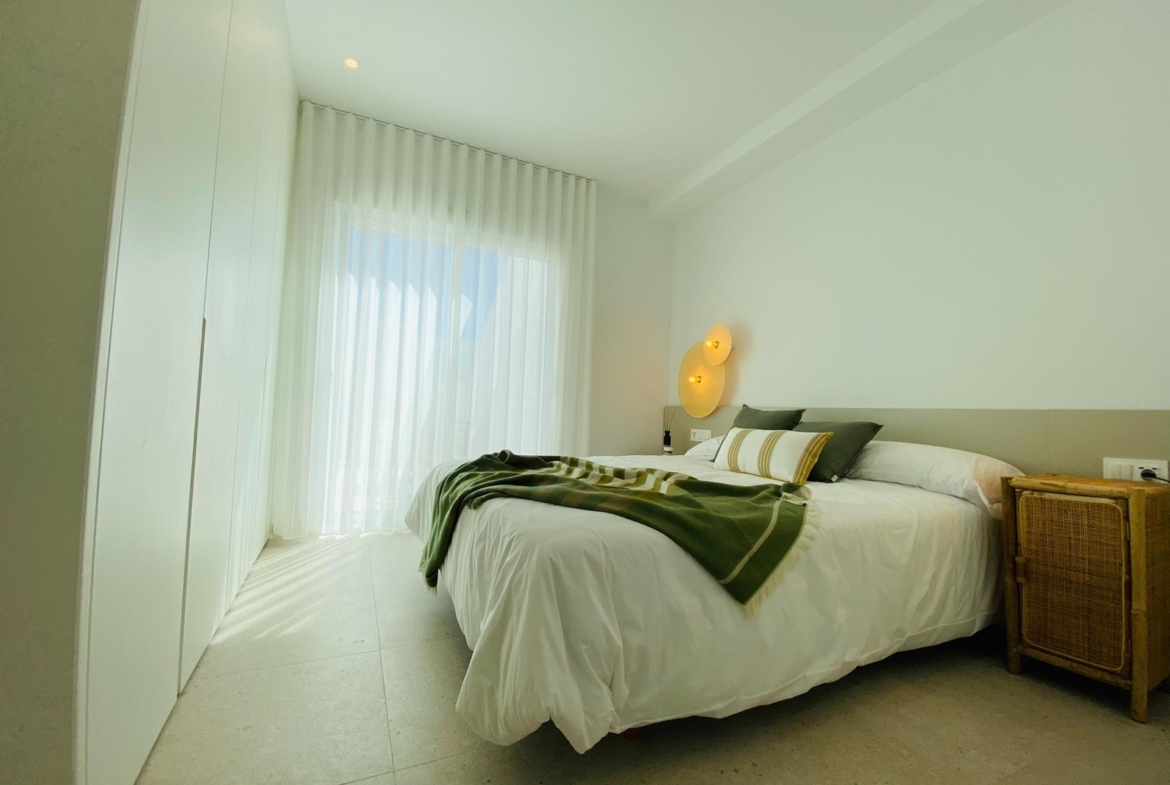 Bedroom with white fitted wardrobes, sheer curtains and bed dressed with green throw