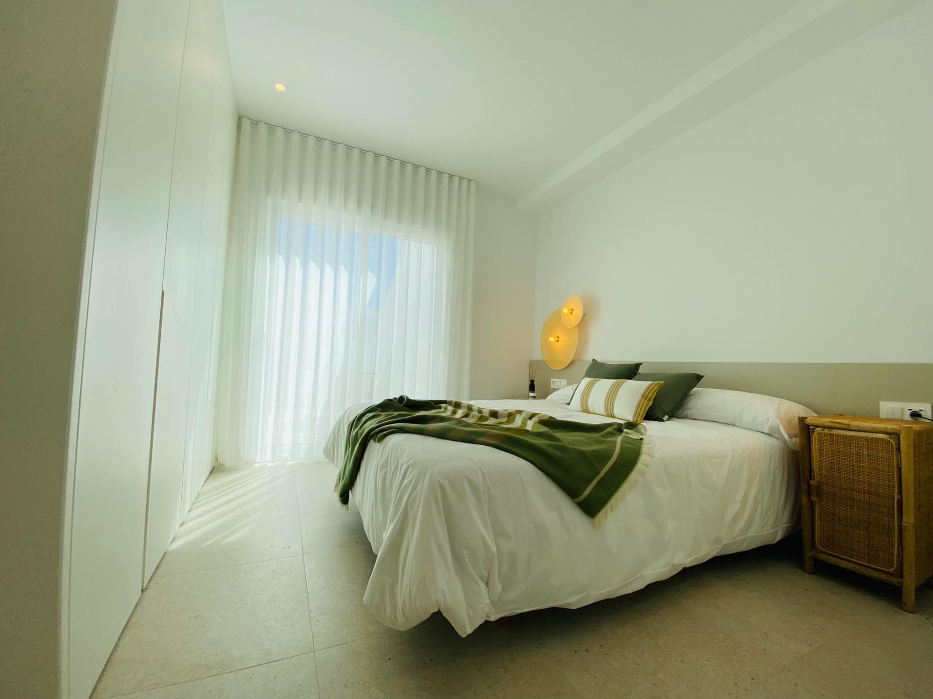 Bedroom with white fitted wardrobes, sheer curtains and bed dressed with green throw