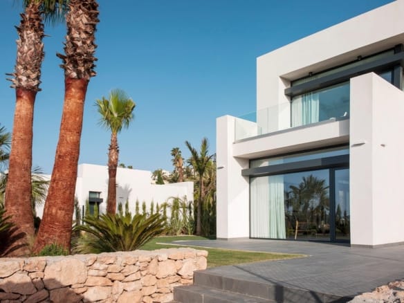 Modern white villa exterior with large glass doors, upper terrace and landscaped garden in La Manga Club, Murcia
