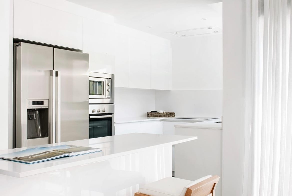 Minimalist white kitchen with breakfast bar and integrated appliances in La Manga Club, Murcia