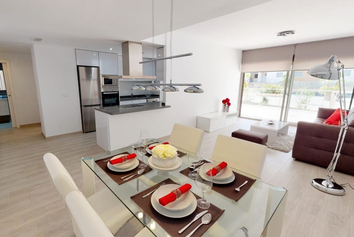 Representative show apartment kitchen and dining area with white cabinetry and terrace glazing, illustrating finishes for homes in San Miguel de Salinas, Alicante