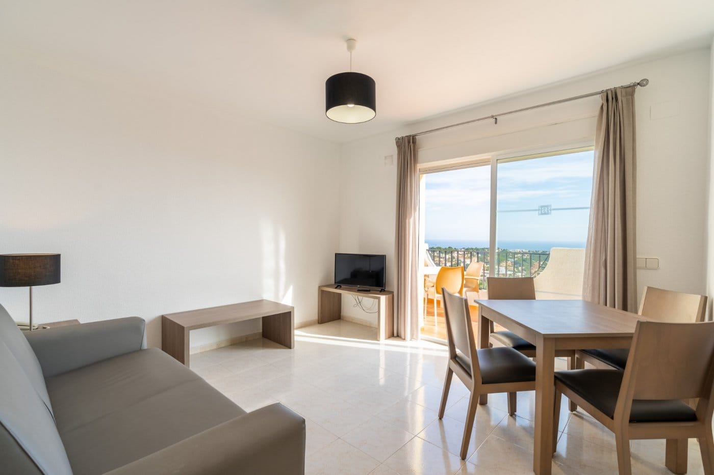 Living and dining room with a grey sofa and sliding doors opening onto a sea-view terrace in Gran Sol, Calpe, Alicante