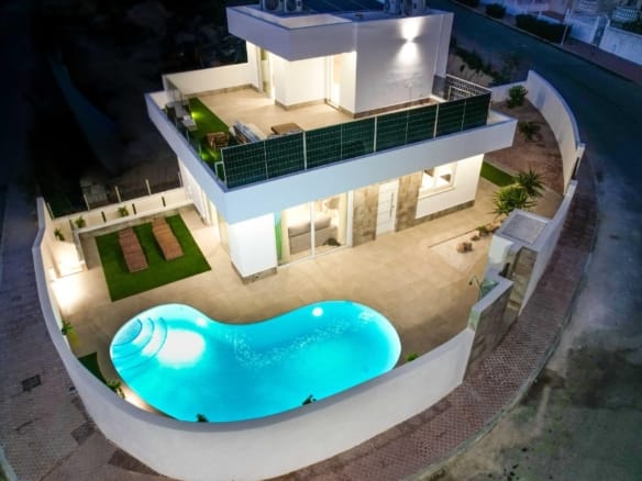 Evening aerial view of a corner villa with an illuminated curved private pool in La Marquesa, Ciudad Quesada, Alicante