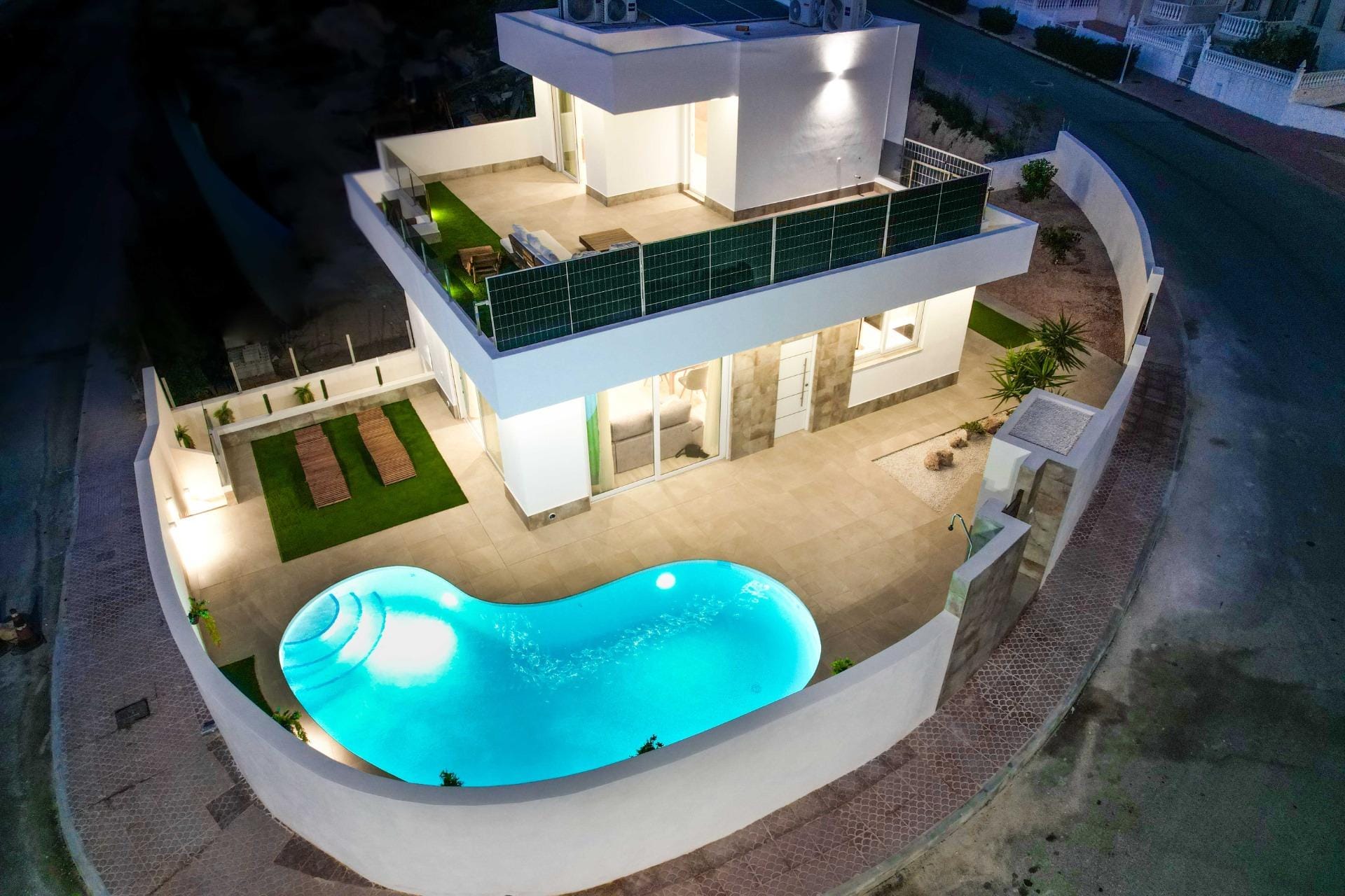 Evening aerial view of a corner villa with an illuminated curved private pool in La Marquesa, Ciudad Quesada, Alicante