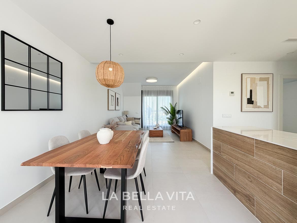 Modern Resale Apartment fot sale in Lo Romero Golf, Pilar de la Horadada, Alicante-15 Wooden dining table and kitchen peninsula with the lounge and terrace doors beyond