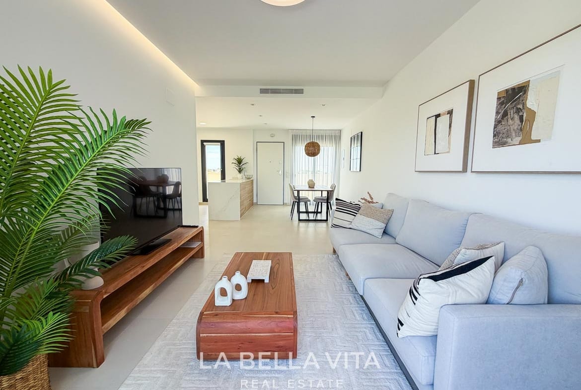Living area with a pale sofa and wooden TV cabinet, looking towards the kitchen and dining space