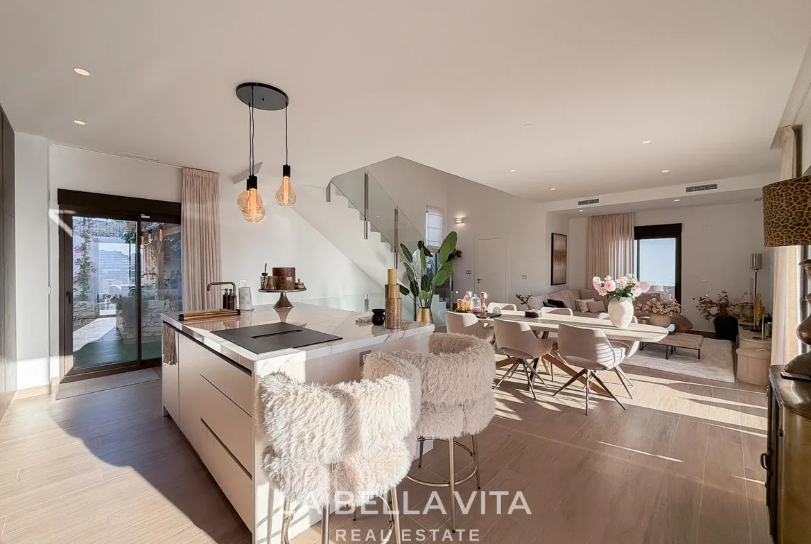 Kitchen island with breakfast stools opening onto the dining area and glass staircase in Finestrat, Alicante.