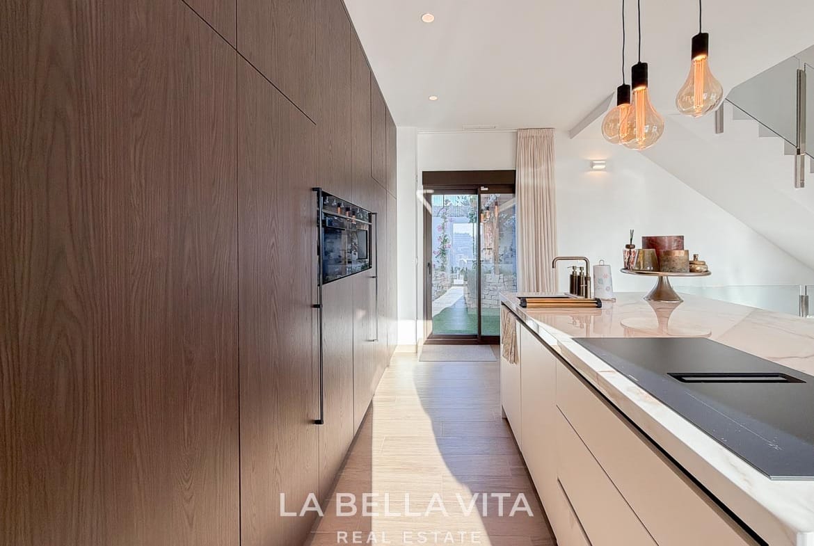 Kitchen aisle between the tall cabinets and island, leading towards the pergola in Finestrat, Alicante.