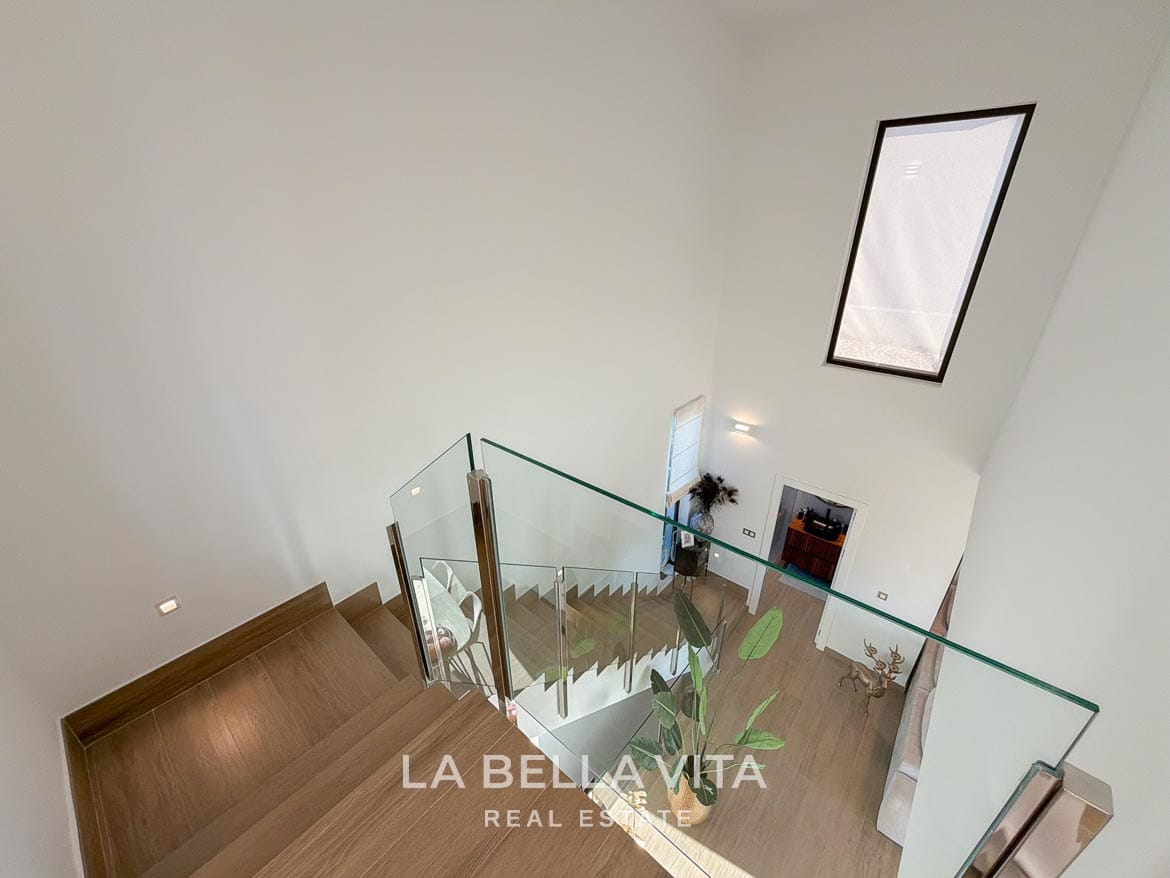 Modern Resale Villa with Basement and Private Pool for Sale in Finestrat-28 View down the staircase with glass balustrades and a tall window in Finestrat, Alicante.