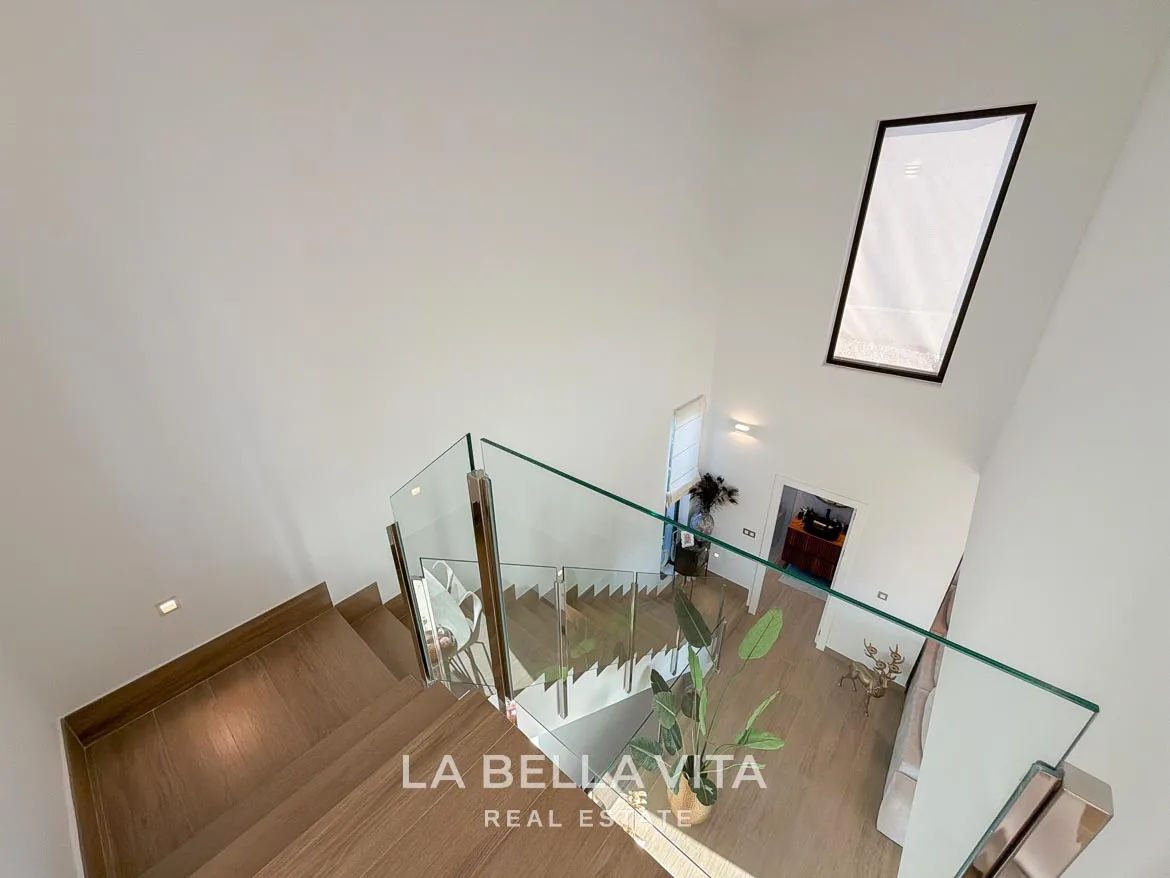 Modern Resale Villa with Basement and Private Pool for Sale in Finestrat-28 View down the staircase with glass balustrades and a tall window in Finestrat, Alicante.