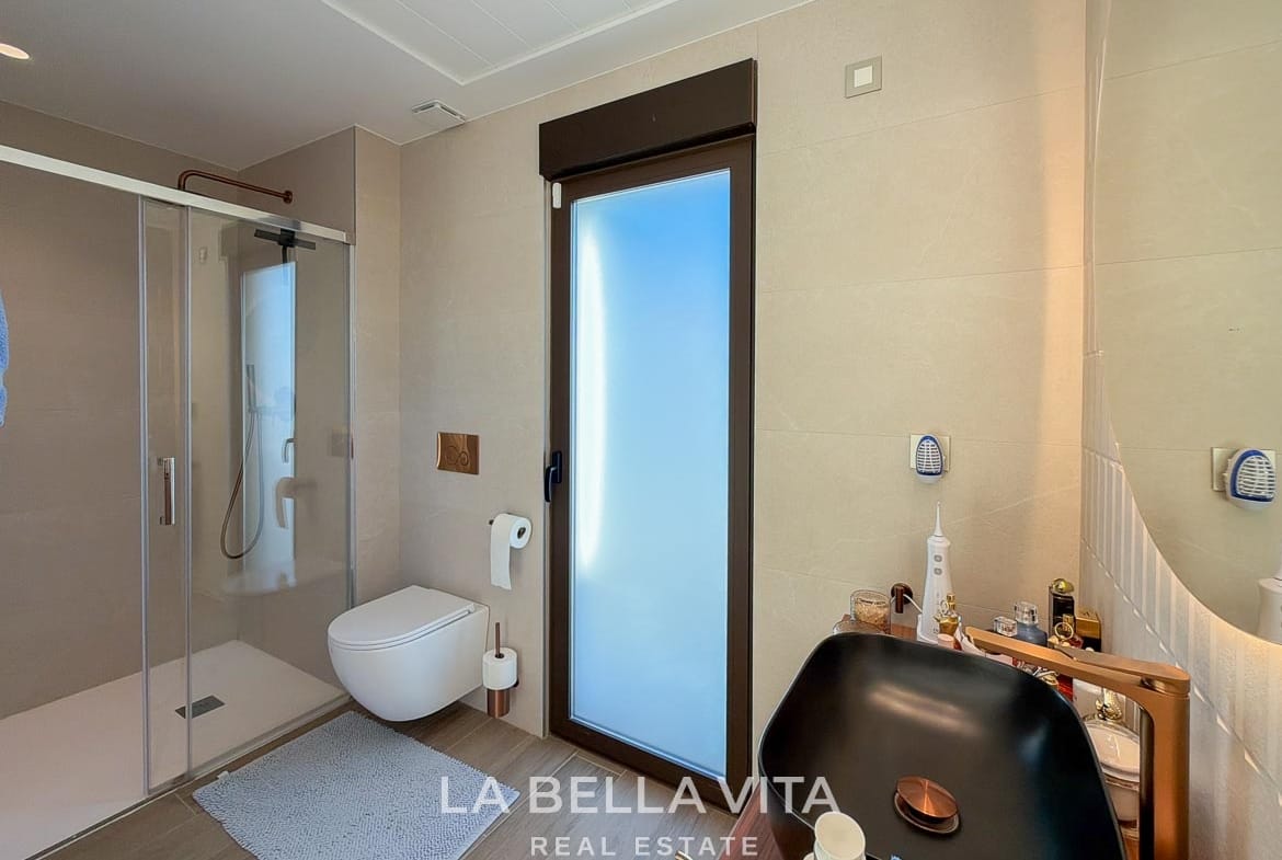 Bathroom with a glass shower enclosure, wall-hung toilet and tall frosted window in Finestrat, Alicante.
