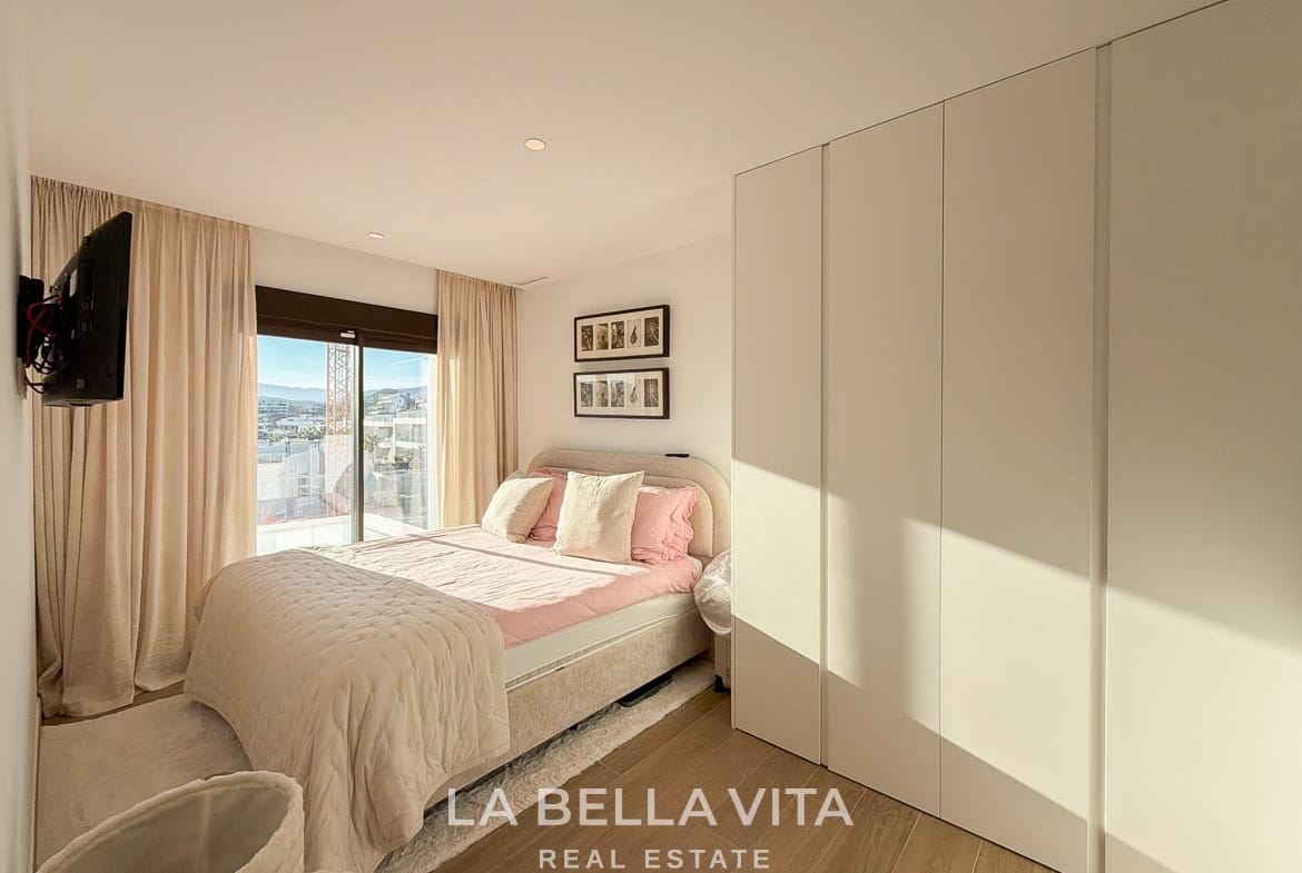 Bedroom with pink bedding, fitted white wardrobes and sliding terrace doors in Finestrat, Alicante.