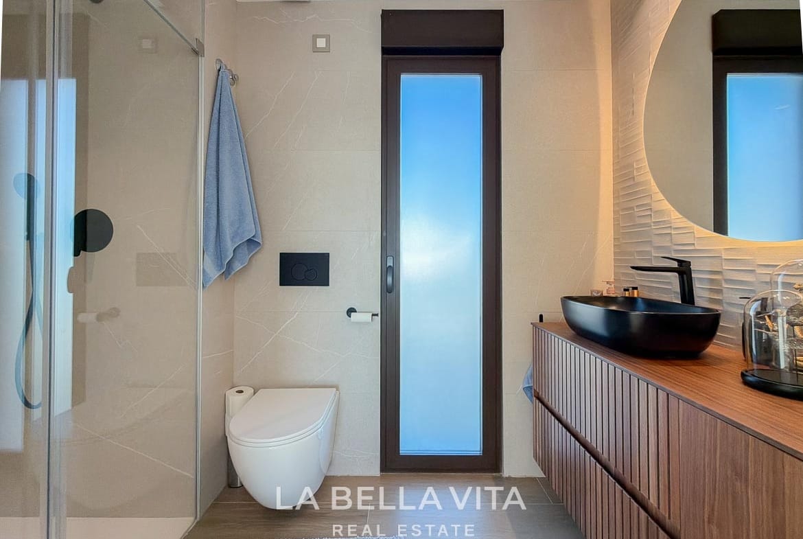 En-suite shower room with a wooden vanity, black basin and frosted window in Finestrat, Alicante.