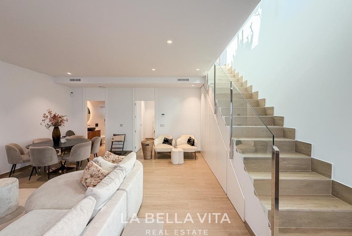 Basement living and dining area beside the glass-balustrade staircase in Finestrat, Alicante.