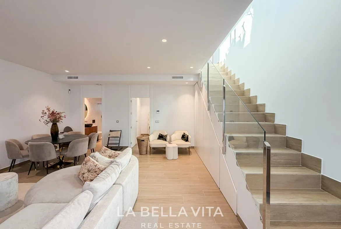 Basement living and dining area beside the glass-balustrade staircase in Finestrat, Alicante.