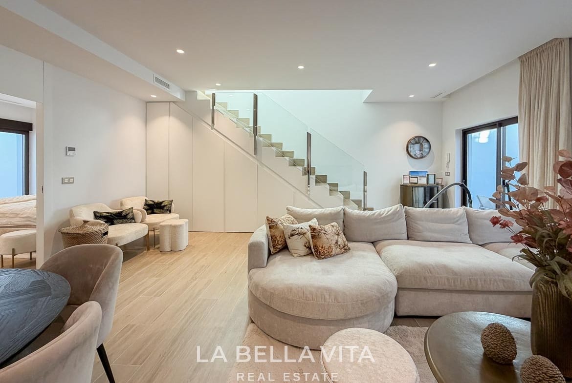 Basement seating area with a curved sofa and fitted storage beneath the stairs in Finestrat, Alicante.
