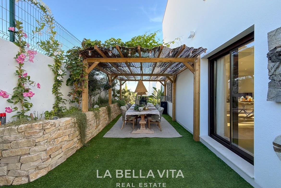 Garden dining area beneath a pergola beside stone planter walls in Finestrat, Alicante.
