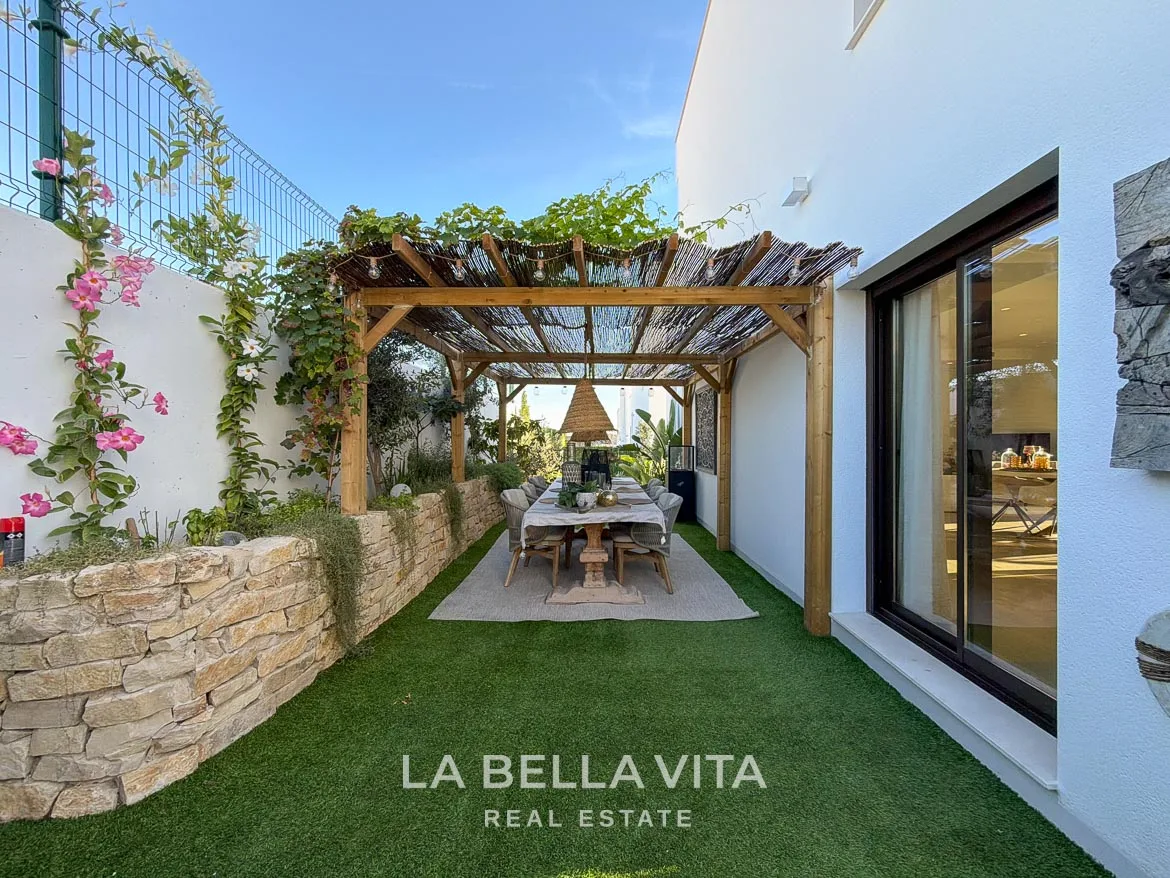 Modern Resale Villa with Basement and Private Pool for Sale in Finestrat-9 Garden dining area beneath a pergola beside stone planter walls in Finestrat, Alicante.