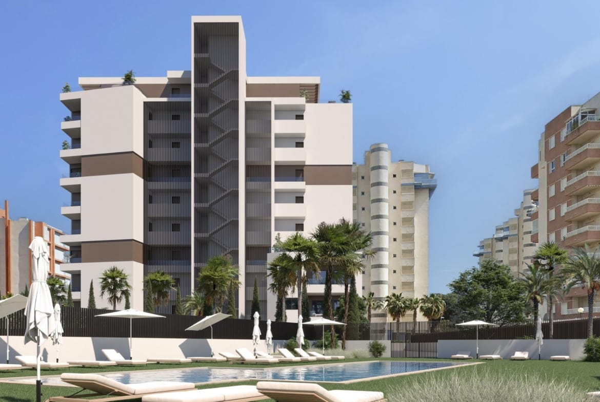 Communal swimming pool with sunloungers and lawns beside a modern apartment building in Guardamar del Segura, Alicante